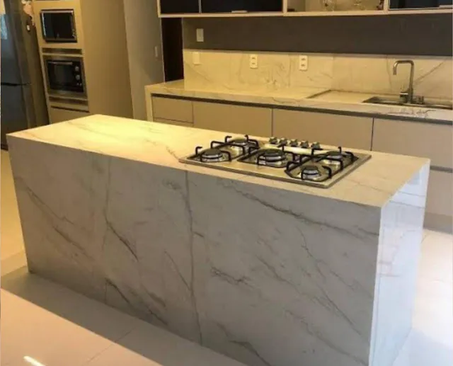 Ilha de cozinha em quartzito branco com veios cinza e cooktop embutido.